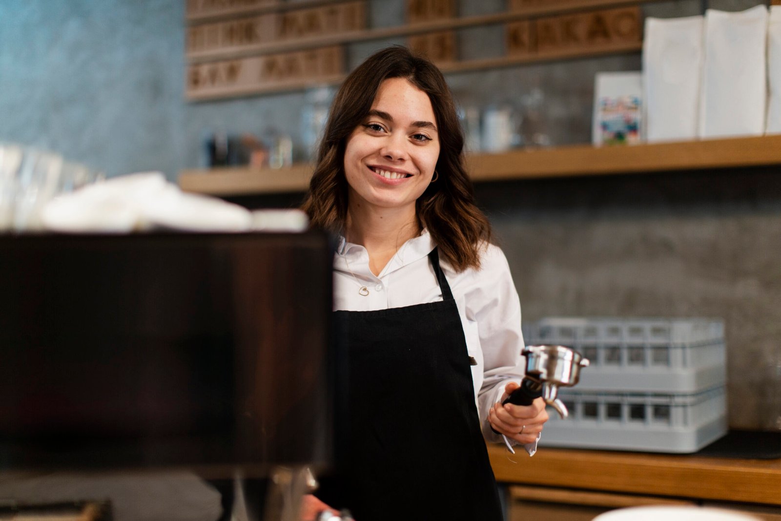 mujer con delantal posando con componente de maquina de cafe